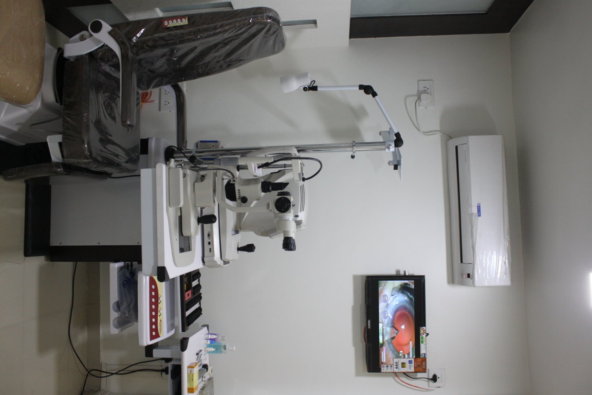 Overhead vantage of an Insight Institute slit-lamp examination station with operating microscope arm, patient chair and surgery demonstration monitor